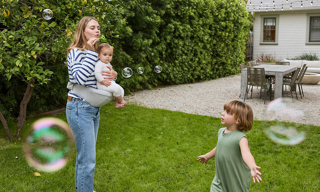 Maman jouant avec ses enfants et portant son bébé avec le Porte-bébé Lift Hip Seat